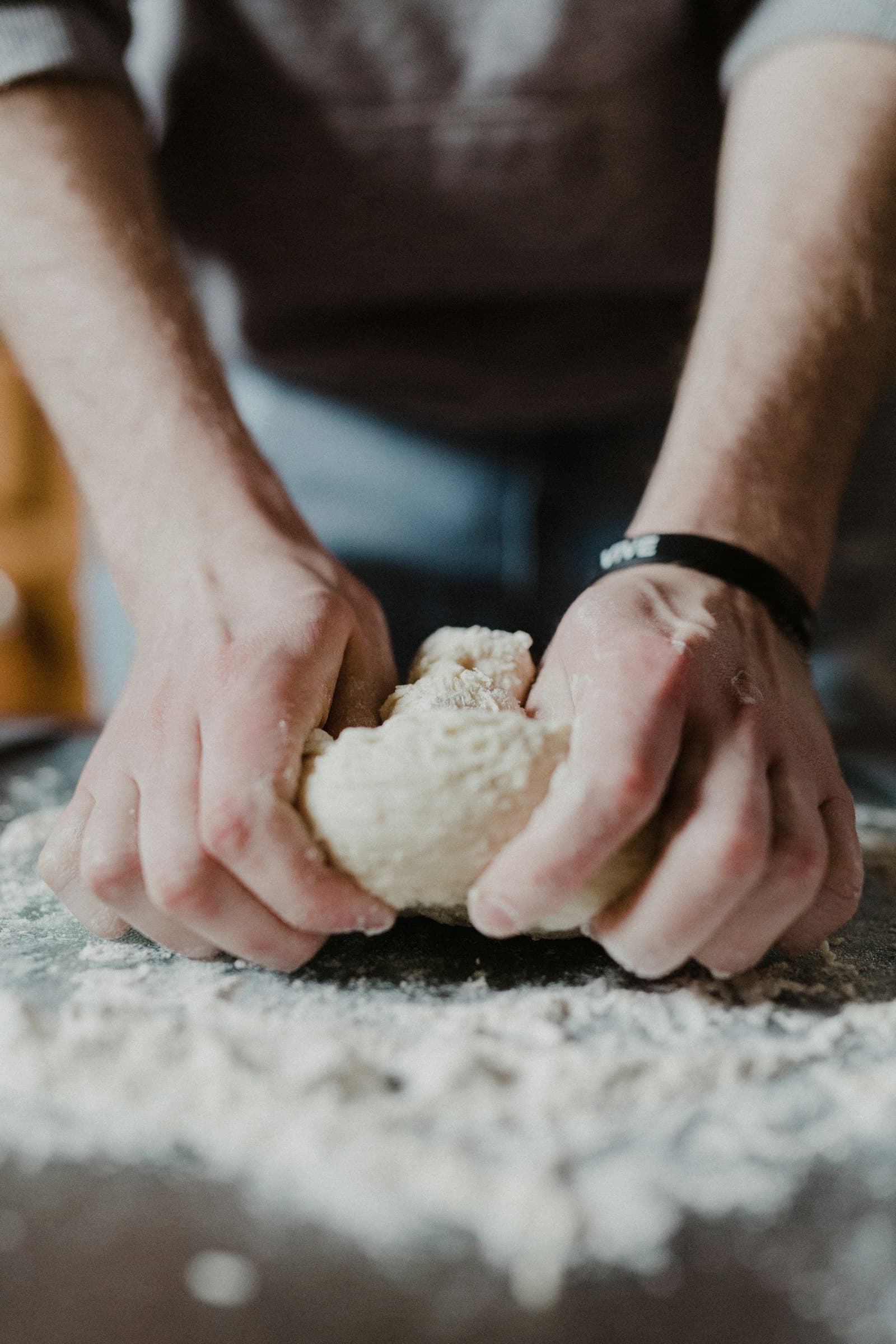 Hands kneading a ball of dough on a floured, dimly lit table