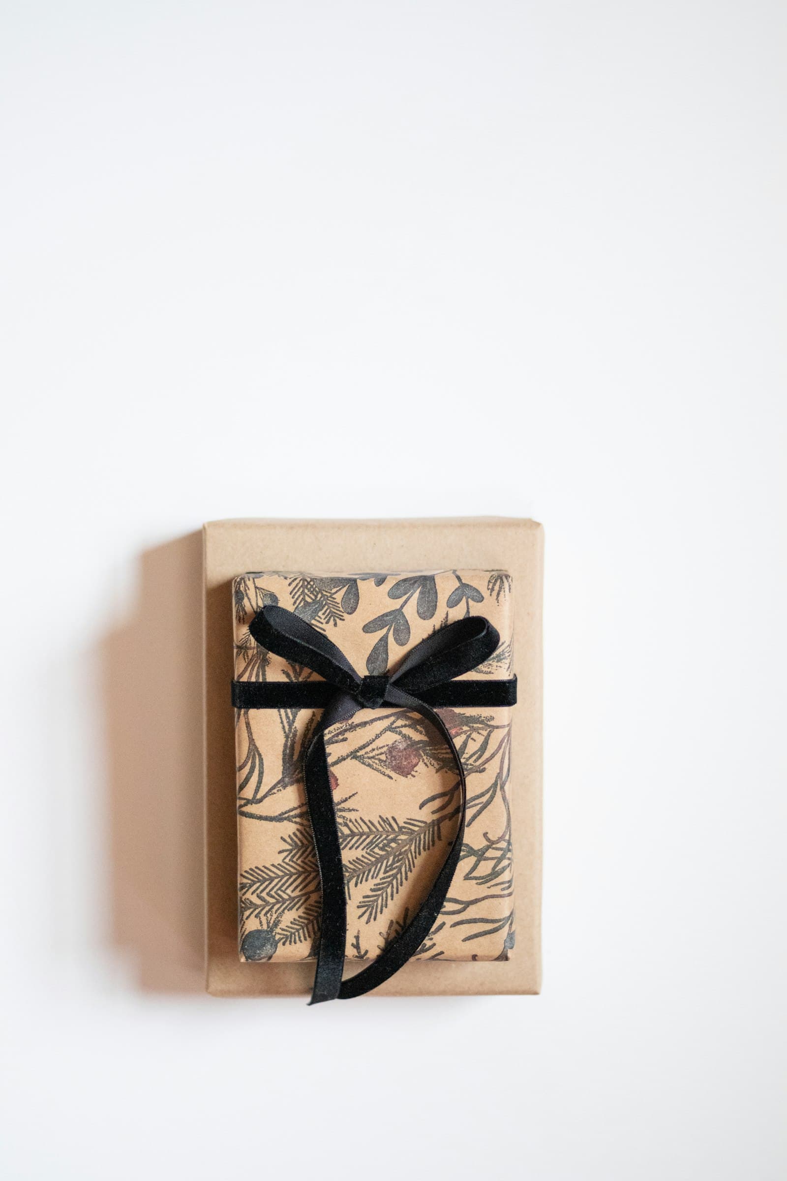 A kraft-paper wrapped gift box with a botanical print, tied with a black velvet ribbon bow