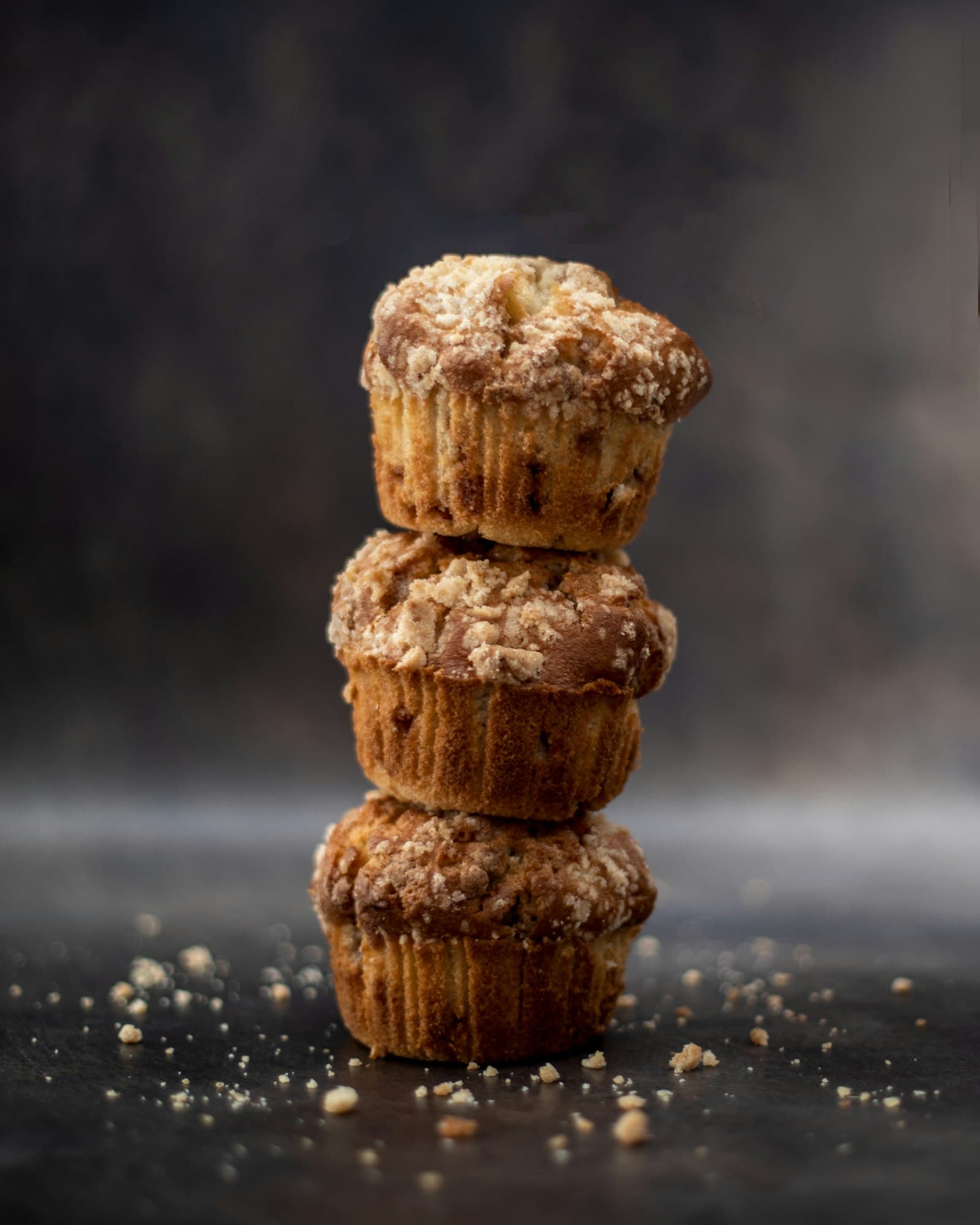Three stacked rustic streusel-topped muffins on a dark, moody surface